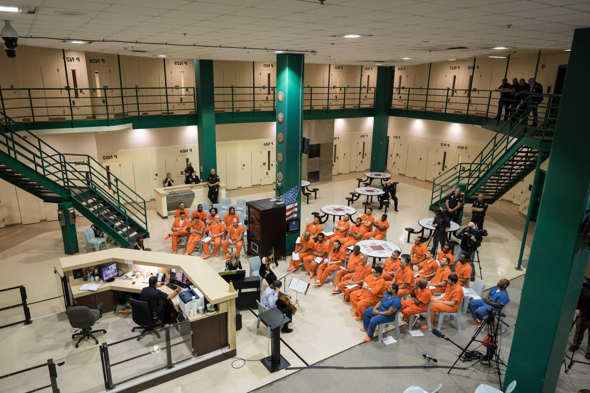 Overhead view of incarcerated people in orange jumpsuits seated for a performance by the ROC城市演唱会 musicians.